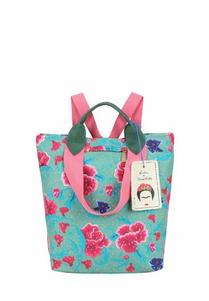 Borsa tote colorata con motivo floreale rosa, manici verdi, spallacci rosa e un'etichetta con un volto stilizzato che indossa una corona di fiori.