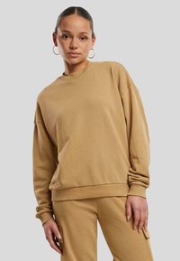 Oversized Sweatshirt aus weichem Material, mit gerippten Bündchen und Saum. Präsentiert mit passenden Hosen, vor einem grauen Hintergrund.
