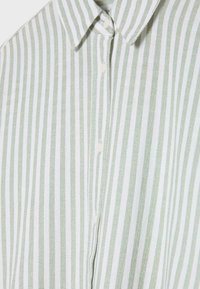 Chemise boutonnée à rayures verticales vertes et blanches avec des boutons blancs et un col pointu, présentée à plat et en gros plan.