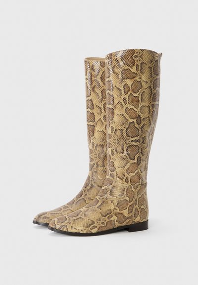 Kozaki sięgające kolan w wzór skóry węża, wykonane z błyszczącego materiału syntetycznego, z szpiczastym noskiem i płaską podeszwą. Kolorystyka obejmuje beżowy i brązowy.