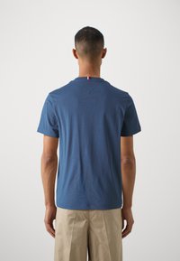 Maglietta in cotone blu scuro con collo a giro e maniche corte, caratterizzata da una piccola striscia rossa, bianca e verde sul retro del collo.