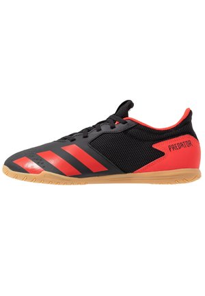 Czarno-czerwony but do piłki nożnej halowej z gumową podeszwą, siateczkowymi bokami, czerwonymi paskami Adidas z przodu oraz napisem "PREDATOR" na pięcie.