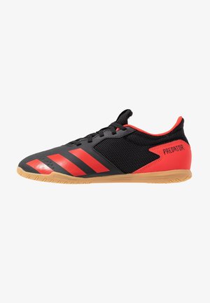 Czarno-czerwony but do piłki nożnej halowej z gumową podeszwą, siateczkowymi bokami, czerwonymi paskami Adidas z przodu oraz napisem "PREDATOR" na pięcie.
