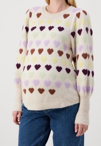 Pull en maille crème avec des cœurs duveteux multicolores en violet, marron, vert, jaune et lavande. Poignets et ourlet côtelés. Coupe décontractée.