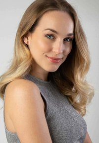 Femme aux longs cheveux blonds ondulés, portant un haut sans manches en gris métallique. Un léger éclat et une texture rehaussent les détails du vêtement.