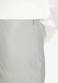 Pantalones de cuero gris claro con una textura suave y un corte ajustado, que presentan un discreto cierre lateral con cremallera.