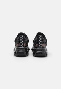 Zapatos deportivos negros con acabado brillante, detalles de malla, tiradores distintivos en la parte trasera y suelas texturizadas. Presentan un diseño moderno con materiales en capas.