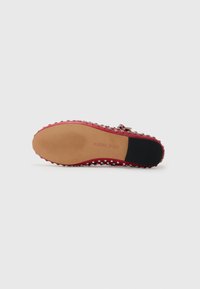 Zapato rojo con una suela de goma flexible, adornado con tachuelas plateadas a lo largo del lateral y una base texturizada para un mejor agarre.