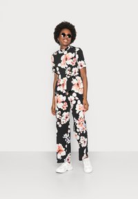 Conjunto floral de duas peças com um fundo preto e flores rosas e brancas. A parte de cima tem mangas curtas e um design peplum; as calças são largas.