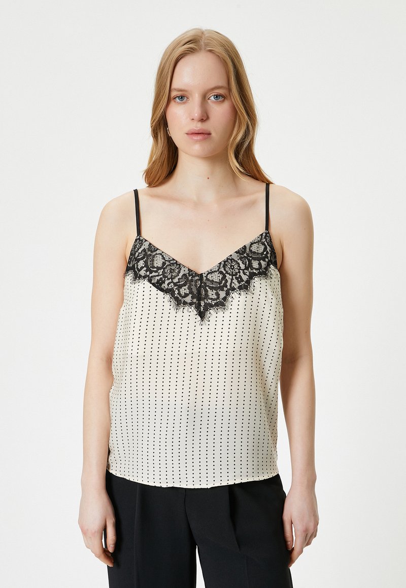 Camisola de satén en color crema con lunares negros, que presenta un escote en V con bordado de encaje. Tirantes finos ajustables y un corte holgado.