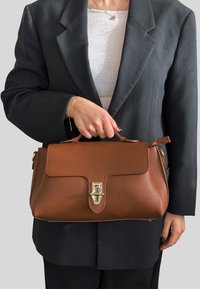 Brązowa torebka ze skóry o fakturze zapięta na złote zapięcie, o zwartej formie, z górnymi uchwytami i dodatkową boczną kieszenią na zamek.