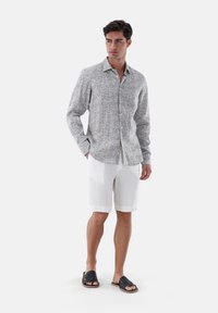 Camicia a maniche lunghe, grigia chiara, con un motivo paisley, abbinata a pantaloni corti bianchi in lino e sandali scuri.