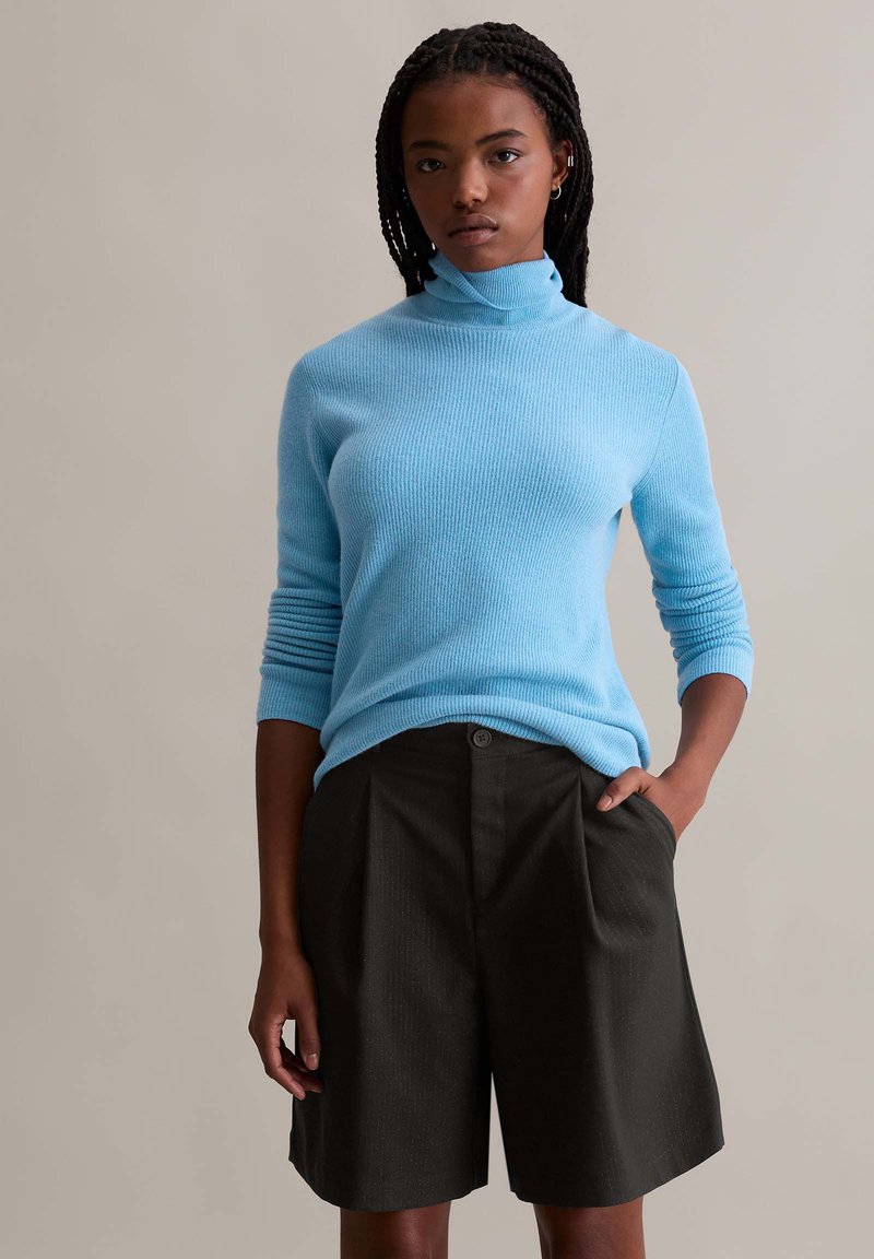 Light blue ribbed turtleneck sweater with long sleeves paired with dark gray pleated shorts featuring a button closure and side pockets.
