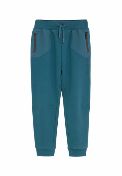 Tyrkysové tepláky vyrobené z mäkkej tkaniny, s bočnými vreckami na zips, rebrovanými manžetami a jemným logom na prednej strane.