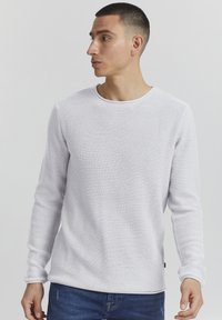 Weißes, strukturiertes Langarmshirt mit Rundhalsausschnitt. Der Stoff hat ein dezentes, gewebtes Muster. Kombiniert mit blauen Jeans.