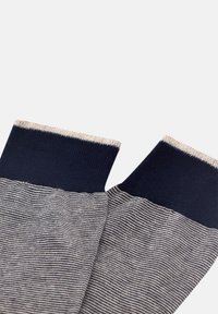 Námořnické a béžové pruhované ponožky s žebrovaným lemem; hladká textura, s kontrastními jednotnými námořnickými vrchy a jemným horizontálním vzorem níže.