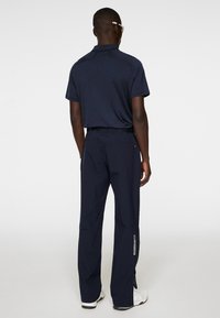 Mörkblå polo t-shirt och matchande byxor med subtil textur. Byxorna har en dragkedja vid nederkant och logotypdetalj på sidan.