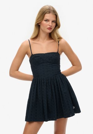 Robe bleu marine avec un corsage ajusté et une jupe évasée, fabriquée dans un tissu texturé avec des broderies florales. Fines bretelles.