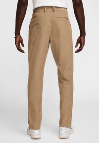 Τα καφέ παντελόνια κοτλέ με ίσια γραμμή, διαθέτουν πίσω τσέπες και λεία υφή. Συνδυάζονται με λευκά αθλητικά παπούτσια.