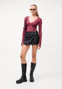 Burgundské body s dlhým rukávom, čierna mini sukňa z faux kože so striebornými detailami a čierne vysoké bojové topánky.