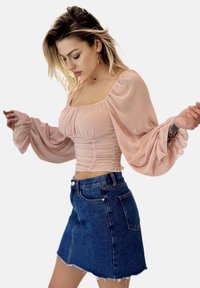 Lichtroze, aansluitend blouse met ballonmouwen en geplooid detail bij de taille. Gepaard met een blauwe denim minirok met een rafelige zoom.