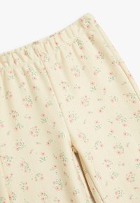 Lichtgele broek met een subtiele visgraatpatroon en een bloemenprint in roze en groen. Elastische tailleband voor comfort.