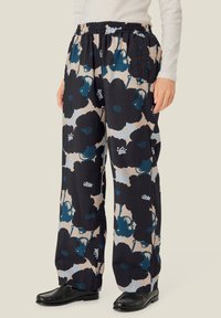Løse bukser i et blomstermønster med store sorte og teal blomster mod en beige baggrund. Elastisk taljebånd, blødt stof.