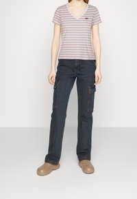 Stribet V-hals T-shirt i lys grå, parret med mørke denim cargo-bukser med sidelommer og brune sko.