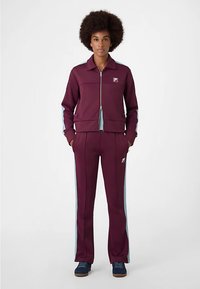 Bordeauxroter Trainingsanzug mit einer Reißverschlussjacke, die kontrastierende hellblaue Seitenpaneele und passende Hosen aufweist. Der Stoff wirkt glatt und hat ein sportliches Design.