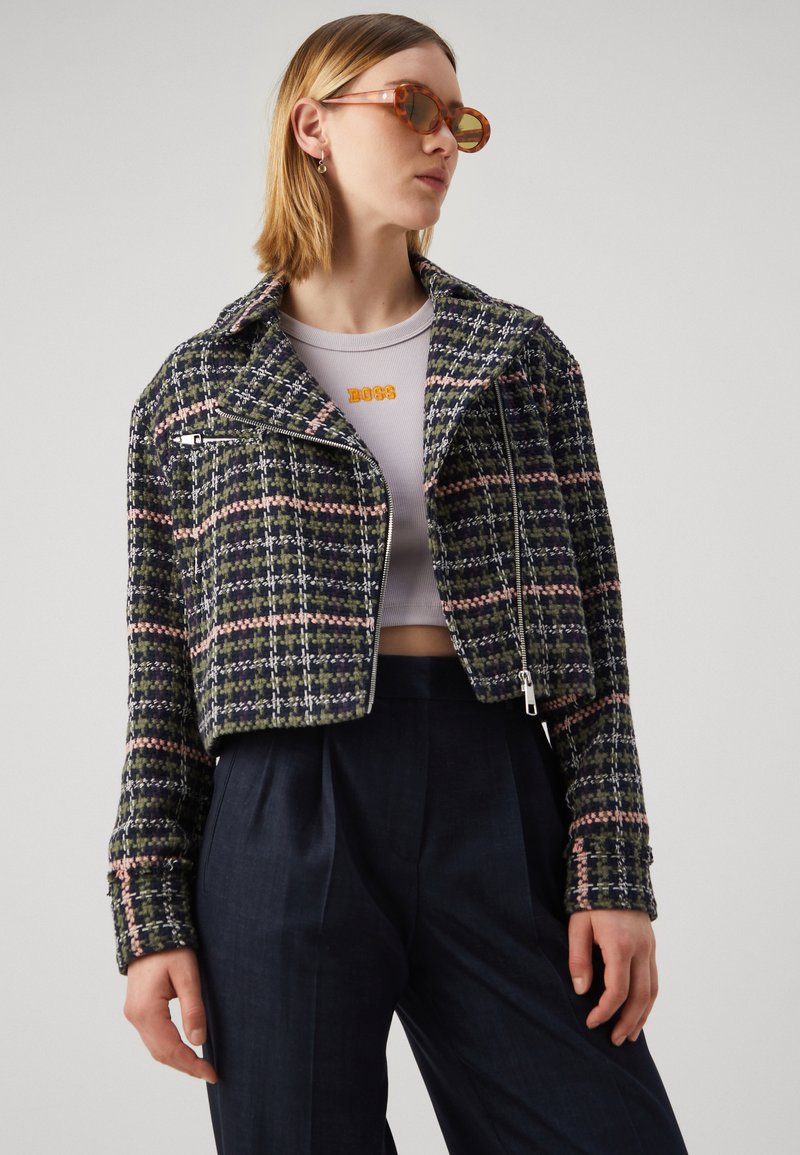 Krótkia kurtka w granatowo-zielonym tweedzie z różowymi akcentami. Posiada wycięty kołnierz, zamek z przodu i dwie boczne kieszenie. Noszona na szarym topie.