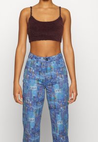 Caraco court bordeaux en tissu duveteux associé à un pantalon bleu à motifs avec des dessins abstraits multicolores, des poches et une fermeture à boutons.