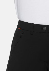 Černé kalhoty s hladkým povrchem, s přední kapsou na zip a oranžovým akcentem u pasu. Zapínání na knoflík s detaily loga.