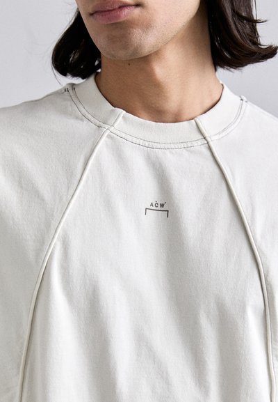 Világosszürke pulóver, bordás kerek nyakkal, a mellkast díszítő diszkrét logónyomattal. Az anyag lágy és textúrált.