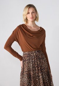 Braunes, langärmliges Oberteil mit elastischem Taillenbund; kombiniert mit einem beige-schwarzen Leopardenmuster-Rock mit Falten und einem lockeren Schnitt.