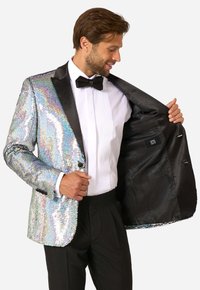 Strieborný lesklý sako s flitrami, čiernymi saténovými klopami a motýlikom. Čierny interiér s vreckami, nosené cez biele košeľové tričko.