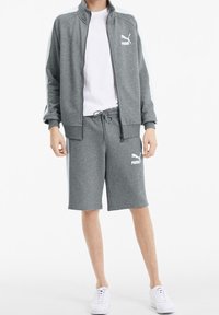 Grijze sportieve trainingspak met een ritsjasje en bijpassende shorts. Heeft een gladde textuur en witte logo-accenten. Gecombineerd met witte sneakers.