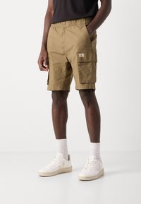 Pantaloni cargo color khaki con cintura elasticizzata, tasche laterali e una tasca frontale con etichetta logo. Texture liscia.