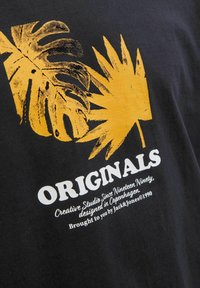 Schwarzes T-Shirt mit gelben abstrakten Blättern und dem Text "ORIGINALS" in Weiß. Weicher Baumwollstoff mit lockerer Passform.
