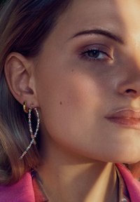 Guldörhängen med hängande, färgglada kristallaccenter. Har en gnistrande design och en avlång form som kontrasterar med den släta hudtexturen.