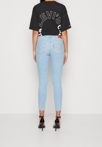 Vaqueros ajustados azul claro con bolsillos traseros y una etiqueta de cuero marrón. Combinados con una camiseta negra extragrande con texto blanco. Tacones altos negros.