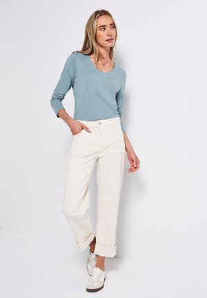 Maglietta azzurra chiara a maniche lunghe abbinata a pantaloni ampi color crema, con polsini arrotolati e scarpe da ginnastica bianche casual con accenti marroni.