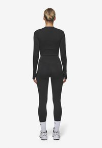 Fekete, hosszú ujjú felső és leggings szett, az alakot követő dizájnnal, sima textúrával és varrat nélküli kivitelezéssel, fehér sportzoknival és cipővel párosítva.