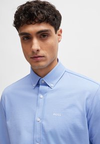 Light blue button-up shirt made of soft fabric. Features a classic collar, white buttons, and a small white "BOSS" logo on the chest.
