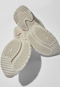 Podeszwa sneakersów w kolorze kremowym, z teksturowaną powierzchnią i charakterystycznym wzorem bieżnika z perforacjami dla lepszej przyczepności i elastyczności.