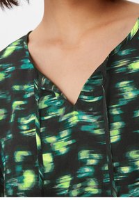 Schwarzer Stoff mit einem grünen und blauen abstrakten Muster, mit einem V-Ausschnitt und subtilen Falten an der Vorderseite. Glatte Textur.