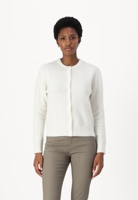 Vitt kofta gjord av mjukt, texturerat material, med rund hals och knappstängning. Långa ärmar och ribbade muddar med en snygg avslutning.
