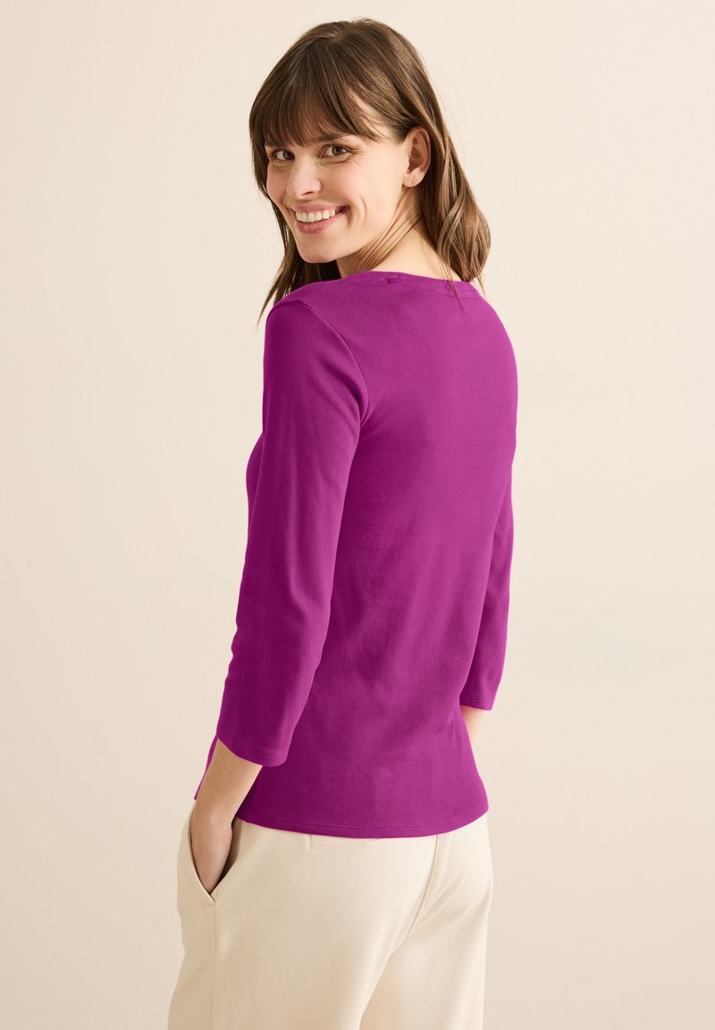 Tajtsittande topp med trekvartsärmar i livlig lila bomull, med rundad halsringning och en något böjd fåll. Enfärgad textur, avslappnad design.
