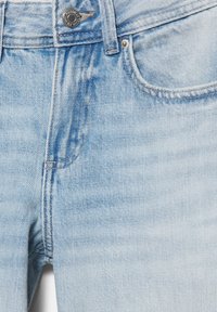 Detaljni prikaz svijetloplavih traperica koji prikazuje gumb, patentni zatvarač, prednji džep i petlju za remen.