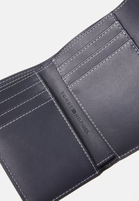 Navy leather wallet with white stitching, featuring card slots and embossed brand name. Smooth texture with a structured design.