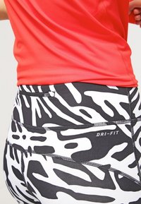 Leggings a strisce zebrate in bianco e nero con un design aderente, dotati di etichetta DRI-FIT e di una piccola tasca con zip sul retro.